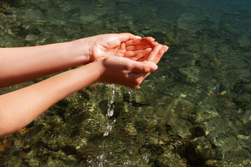 A woman touches the water with her hands. Women's hands collect water in their hands near the...