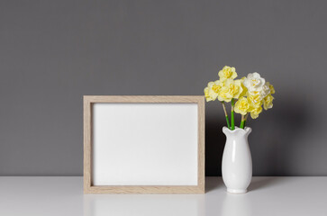 Blank landscape picture frame mockup with daffodils flowers in vase, copy space