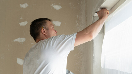 Worker is putting a gypsum plaster on a wall using a spatula. 