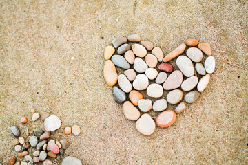 A heart made of rocks on a sandy beach. The heart is surrounded by smaller rocks, creating a unique...
