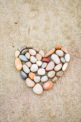 A heart made of rocks on a sandy beach. The heart is made of various colored rocks, including red, brown, and white. Concept of peace and tranquility
