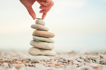 A person is holding a rock on top of a stack of rocks. Concept of balance and stability, as the...