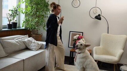 The girl dances in the room and teases the dog, which playfully jumps up with its paws at her.