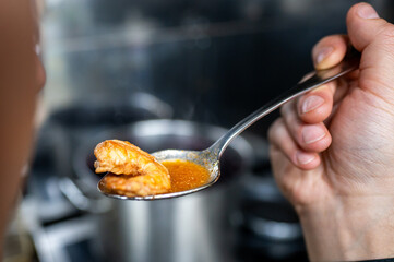 Close-up of a hand holding a spoon with shrimp and soup over a pot, suggesting cooking or food...