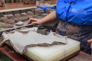 A shoe factory worker cuts pieces of leather from a blank.