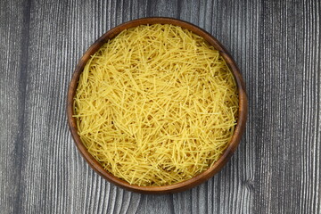 White gluten free vermicelli made from rice flour. Italian pasta in wooden spoon on dark textured...