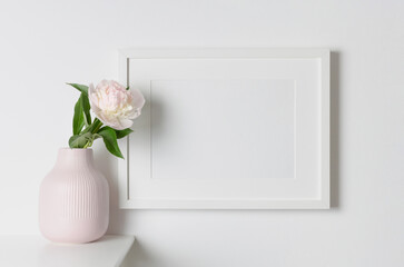 Blank landscape frame mockup on white wall with flowers decor, copy space for artwork