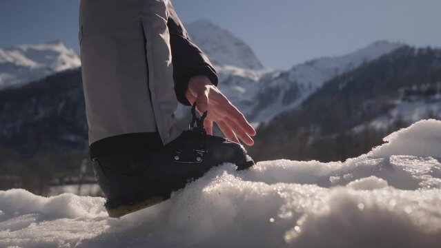 Skier puts his foot with ski shoes on the snow, fastens the fastening. Adjusting boot buckle on ski boot. Ski resort or a slope. Preparation for skiing. Winter sport and holiday. Big mountains