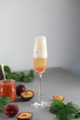 Bellini plums champagne cocktail in crystal glass and fresh fruits on gray table.