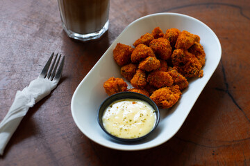 deep fried crispy breaded mushroom on elongated white plate, served with creamy dipping sauce, on wooden table
