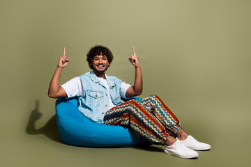 Full length photo of nice young male sit beanbag point up empty space dressed stylish denim garment...