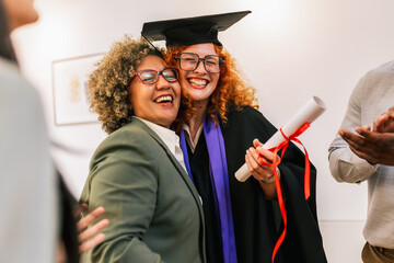 Ginger graduate student in toga celebrating graduation with African American mother.