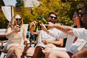 Young group of people drinking beer and having fun by the pool