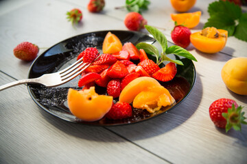 fresh fruit salad of ripe strawberries and apricots, on a light wooden table