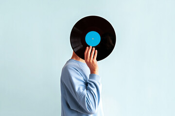 Man in  blue sweatshirt covers his face with vinyl record on blue background