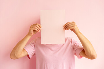 Man covering his face with blank pink sheet of paper.