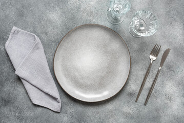 Table setting in gray color. Empty gray plate, cutlery and glasses on a gray background. Top view,...