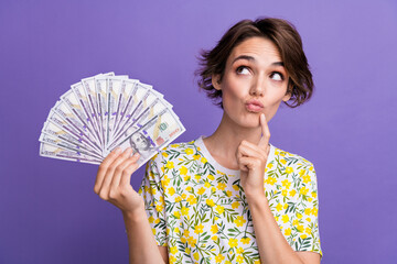 Photo of pretty young woman hold dollar bills look empty space wear t-shirt isolated on violet...