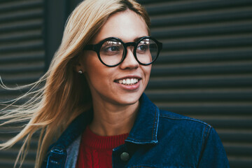 Positive young woman with blonde hair laughing while looking away outdoors.Hipster girl in optical...