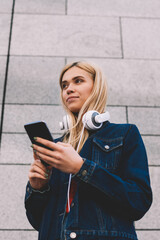 Below view of blonde young woman blogger with modern headphones on neck making payment online on...