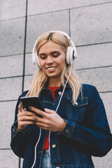 Cheerful blonde young woman downloading music songs on mobile player via 4G internet while...