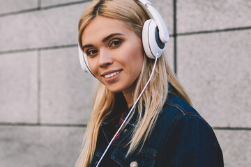 Half length portrait of positive blonde woman enjoying recreation with music while standing against...