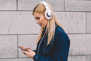 Side view of hipster girl dressed in denim apparel choosing audio songs in music application on...