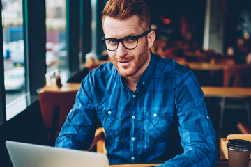 Portrait of handsome successful entrepreneur in eyeglasses looking at camera while working on...