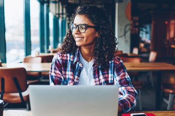 Happy dark skinned female graphic designer in eyewear laughing during working at modern latop...