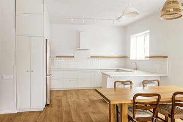 Modern kitchen interior. Stylish white kitchen cabinets with brass knobs, granite counter, appliances and rustic wooden table in new scandinavian house. Modern minimal kitchen design.