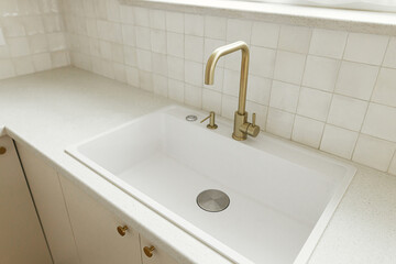 Modern minimal kitchen design. Stylish brass faucet and white granite sink, kitchen cabinets with knobs and granite counter in new scandinavian house.  Modern kitchen interior