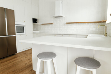 Modern minimal kitchen design. Stylish white kitchen cabinets with brass knobs, faucet, granite island, wooden shelves and appliances in new scandinavian house.  Modern kitchen interior