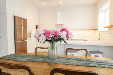 Modern kitchen interior. Beautiful peonies in vase on wooden table on background of stylish white...