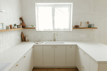 Modern minimal kitchen design. Stylish white kitchen cabinets, brass faucet and granite sink, wooden shelves with utensils  in new scandinavian house.  Modern kitchen interior
