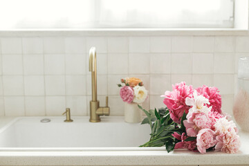 Beautiful peonies in sink on background of brass faucet and white counter in new scandinavian...