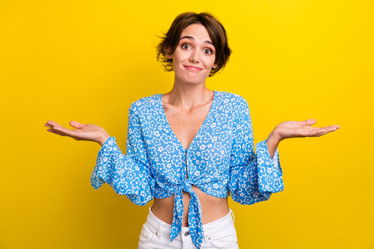 Photo of doubtful unsure young lady dressed flower print top shrugging shoulders isolated yellow color background