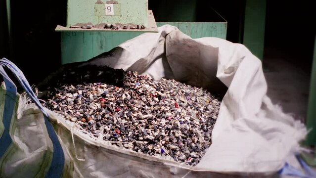 Pieces of plastic fall into a plastic bag. Pile of parts of unprocessed raw materials. Plastic bottle flakes poured into a big bag. Recycling plastic bottles. Polymer granules are used for production