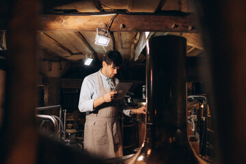 Beer quality control. Man in apron and protective mask with digital tablet looking at glass of beer...