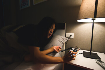 Low-key Woman waking up early in the morning time. drowsy lady pushing smart phone with hand....