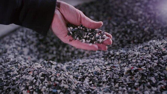 Hand touches the granules of crumb microplastics. Plastic or polypropylene pellets in a bag. Engineer checks or inspects the raw materials for recycling. Polymer granules are poured from the palm.