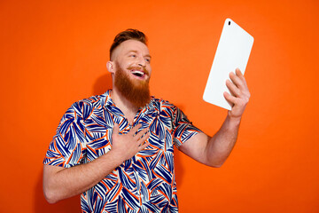 Portrait of friendly handsome man with red long beard look at tablet talk on video call isolated on...