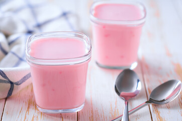 Two portions of homemade fruit pink yogurt in a glass jars on a white table, selective focus.