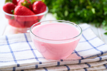 pink smoothie in a clear glass bowl with strawberry on a white table, selective focus.