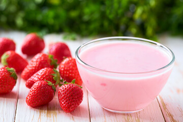 pink yoghurt in a clear glass bowl with strawberry on a white table, selective focus.