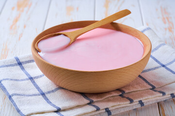 pink fruit yogurt in a wooden bowl with spoon on a light background, selective focus.