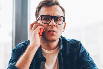 Half length portrait of pondering male student in cool spectacles communicating with friends via...
