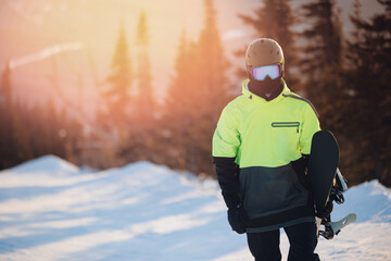 Man snowboarder holding snowboard on background snowy forest with sunset light. Concept trip winter...