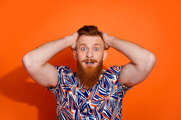 Photo of impressed excited guy dressed print shirt arms head big eyes isolated orange color background