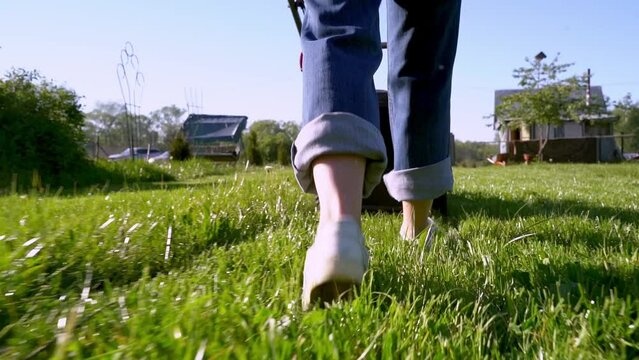 Woman with a lawnmower mows the lawn at the dacha