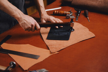 Tailor processing hammers seam on leather goods, handmade craftsman. DIY craft product from skin